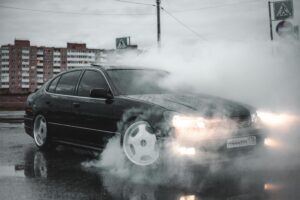 Black car on the roadside with smoke rising from the engine, indicating overheating issues.